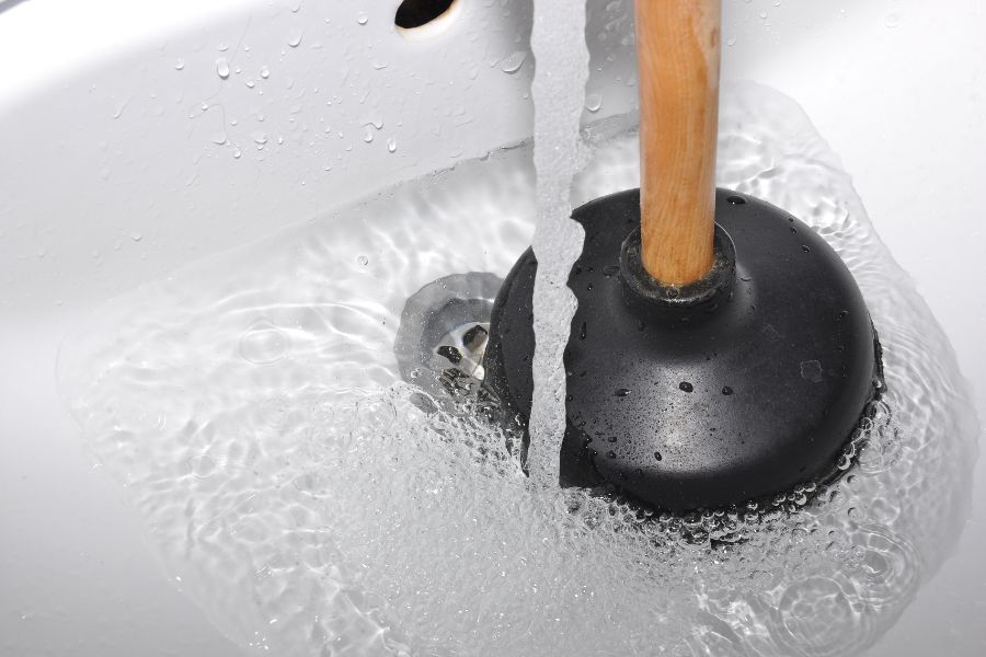 A sink with water running and a black plunger inside of the sink.
