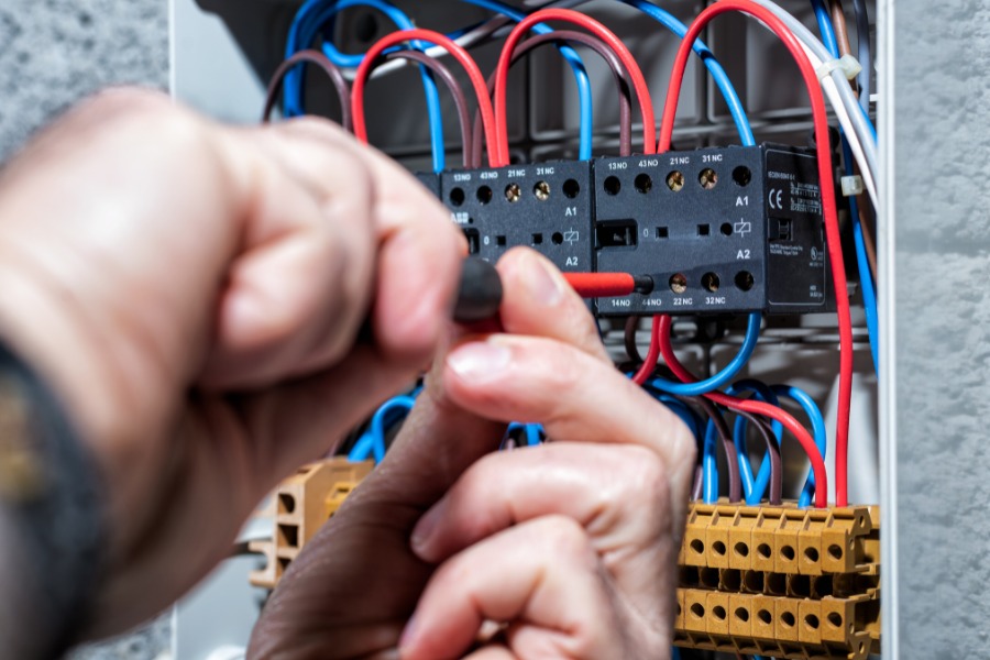 Two hands working in front of an electrical panel.
