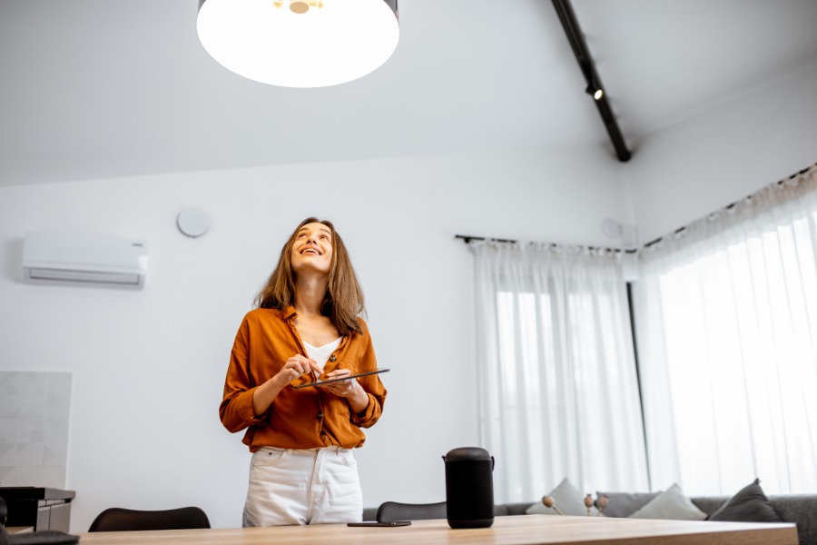 A woman with brown hard and in an orange shirt, standing under a ceiling light fixture.