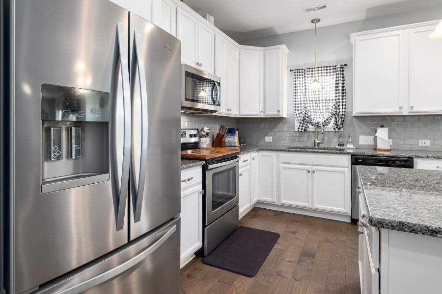 A kitchen with stainless steel appliances, white cabinets, and dark floors.