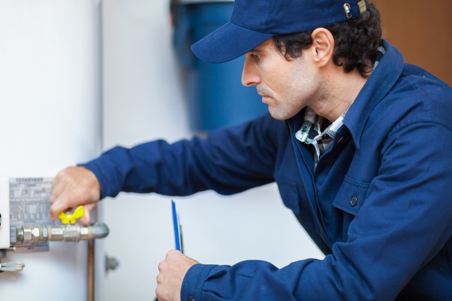 A person who is in a blue hat and work outfit, working on a water heater.