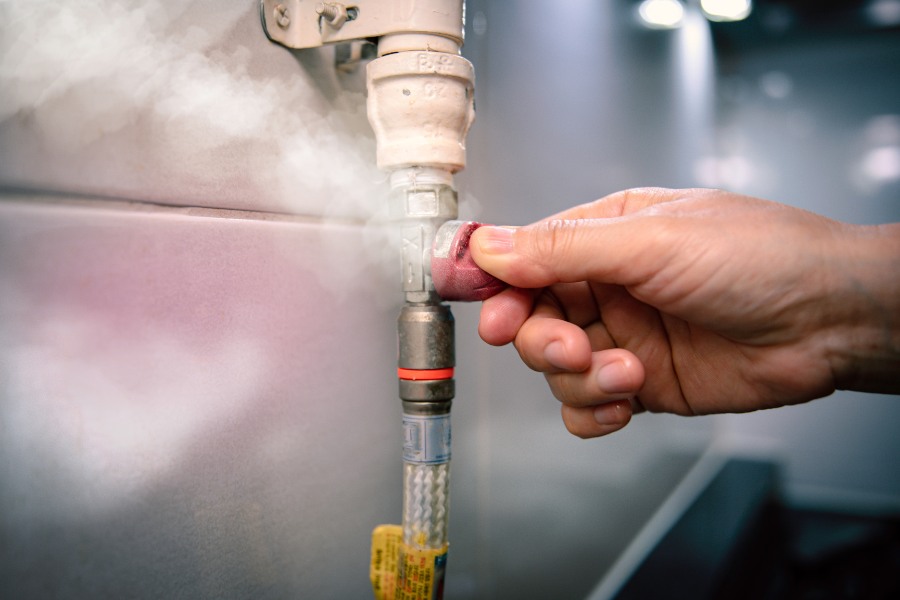 A hand turning a gas pip with steam coming out.