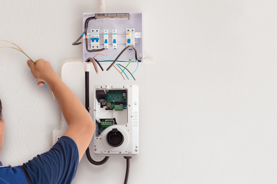 A person installing an EV charging station on a white wall.