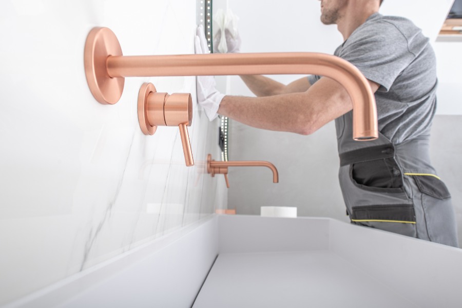 Bathroom faucet fixtures on a white stone wall with a person working behind.