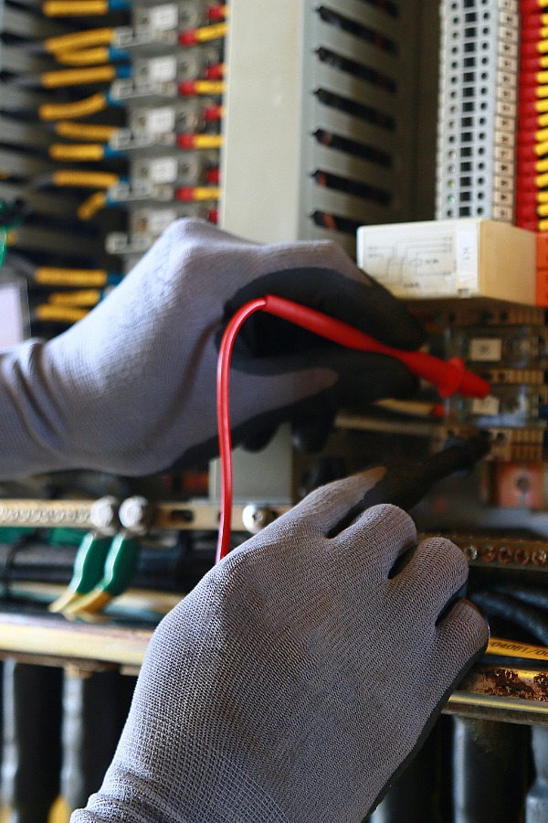Two hands with gloves on working on an electrical panel.