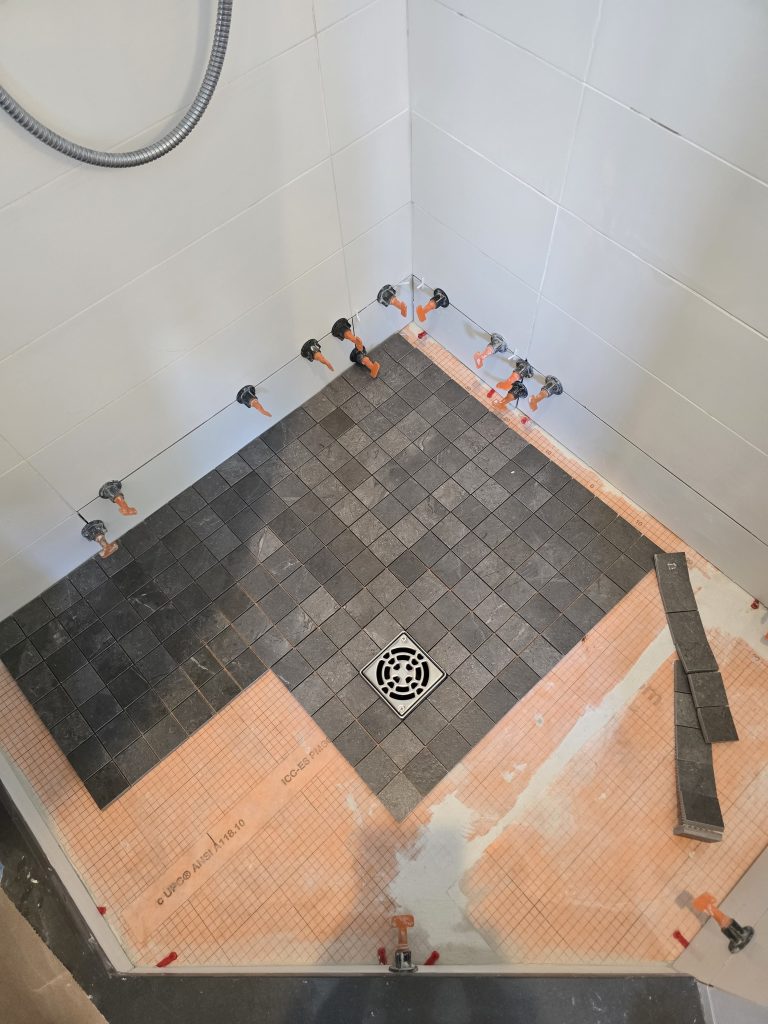 New flooring tile being installed in a corner shower.