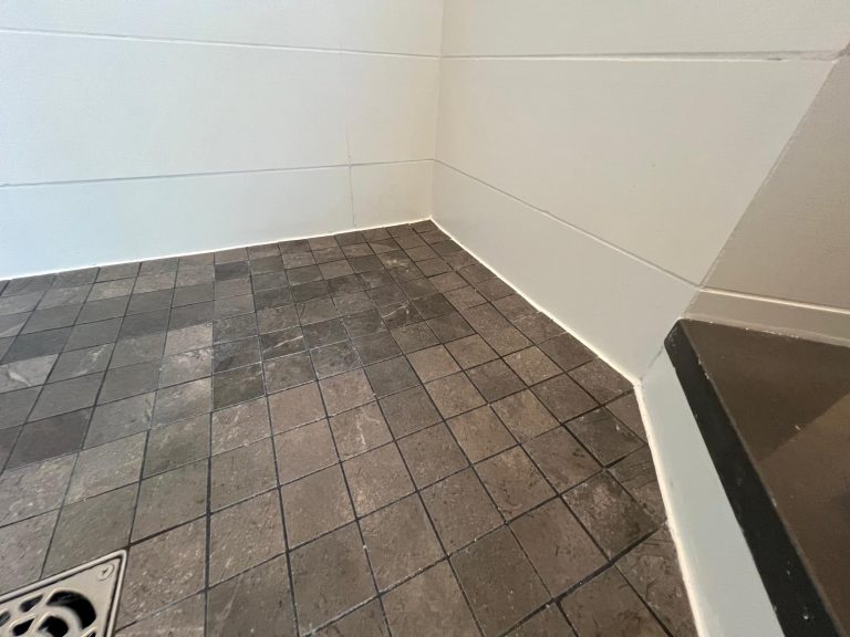 A corner shower with white tile surrounding and new floor tiles.