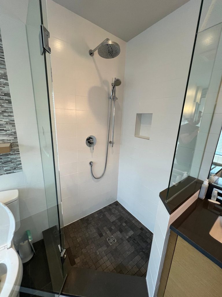 A corner tiled shower, with new floor tiles and a white tile surround.
