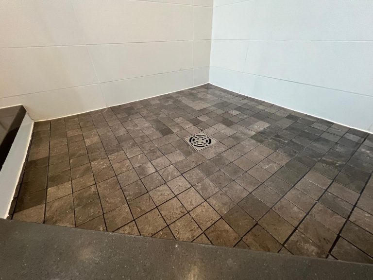 A corner shower with white tile surrounding and new floor tiles.