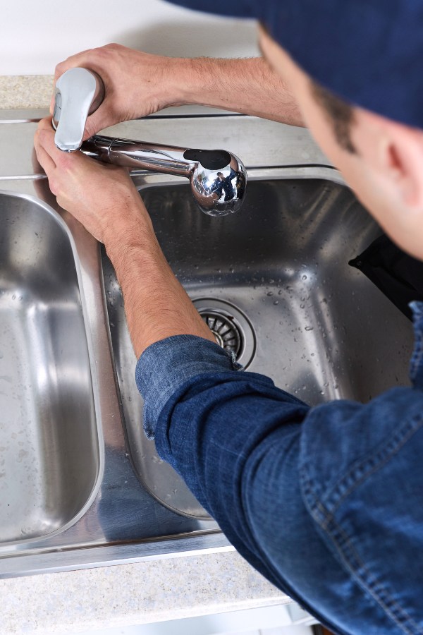 A person in a blue shirt and hat fixing a faucet.